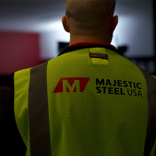 A Majestic Steel associate working in our service center and wearing a safety vest that features Majestic Steel branding